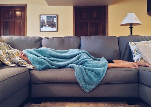 person laying on couch covered by a blanket